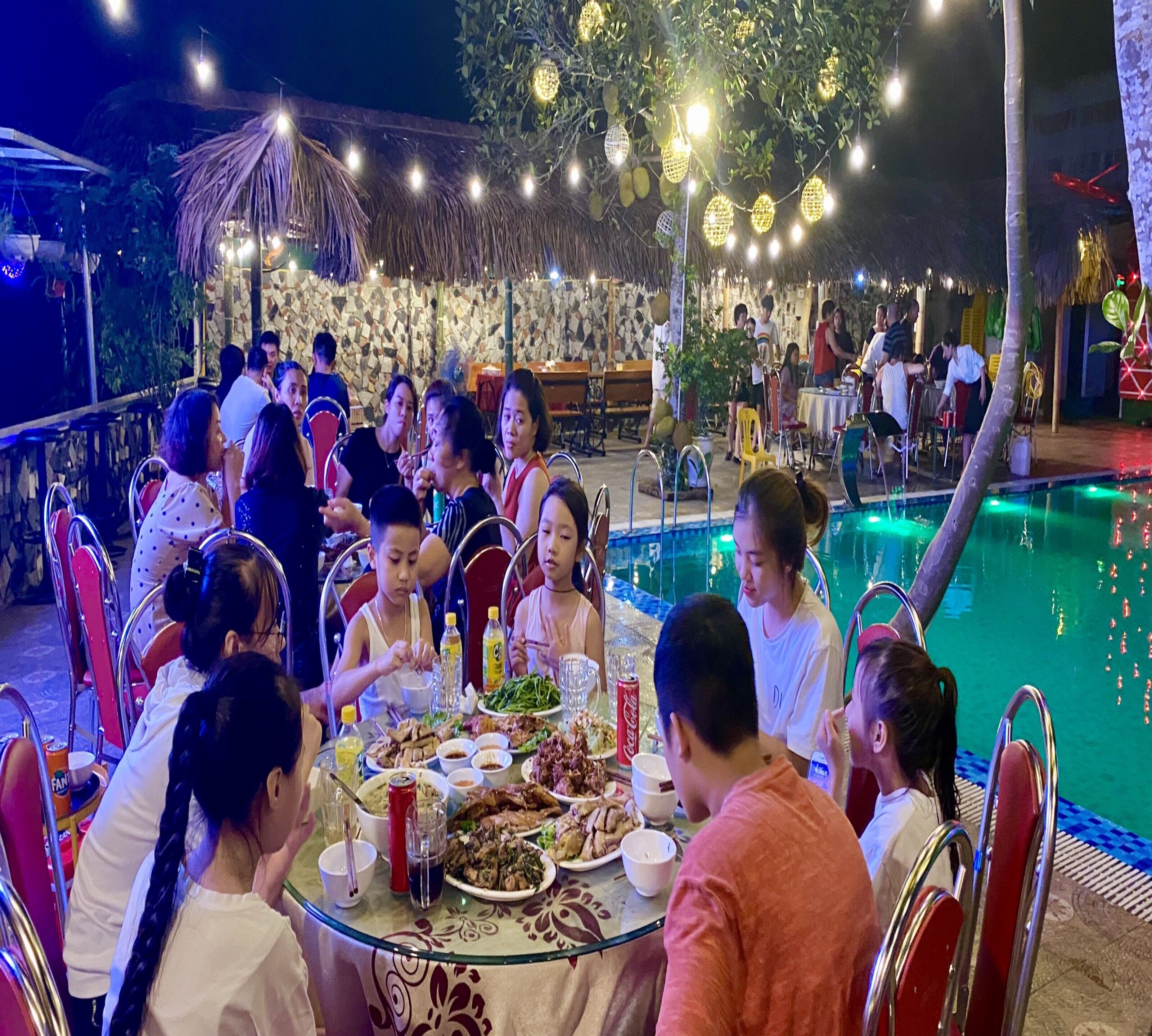 A group of people dining outdoors at a restaurant with a pool.