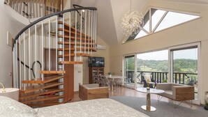 A spacious room with a curved staircase, a large bed, a balcony with a view, and a dining area.