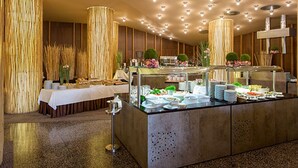 A buffet setup with a variety of food items, a long table with a white tablecloth, and decorative plants.
