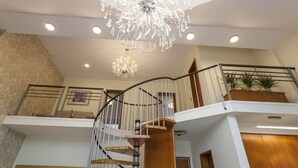 A spacious living area with a modern staircase, a chandelier, and a view of the kitchen.