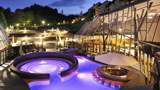 A modern spa with a hot tub, seating area, and a glass building.