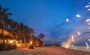 A beachfront property with a wooden deck, palm trees, and a beach chair.