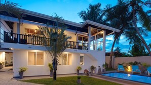 Uma casa moderna de dois andares com piscina, área de estar ao ar livre e palmeiras.