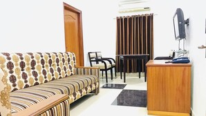 A living room with a sofa, a small table, a chair, a desk, and a television. - NAVEED RESIDENCY (Anantapur)