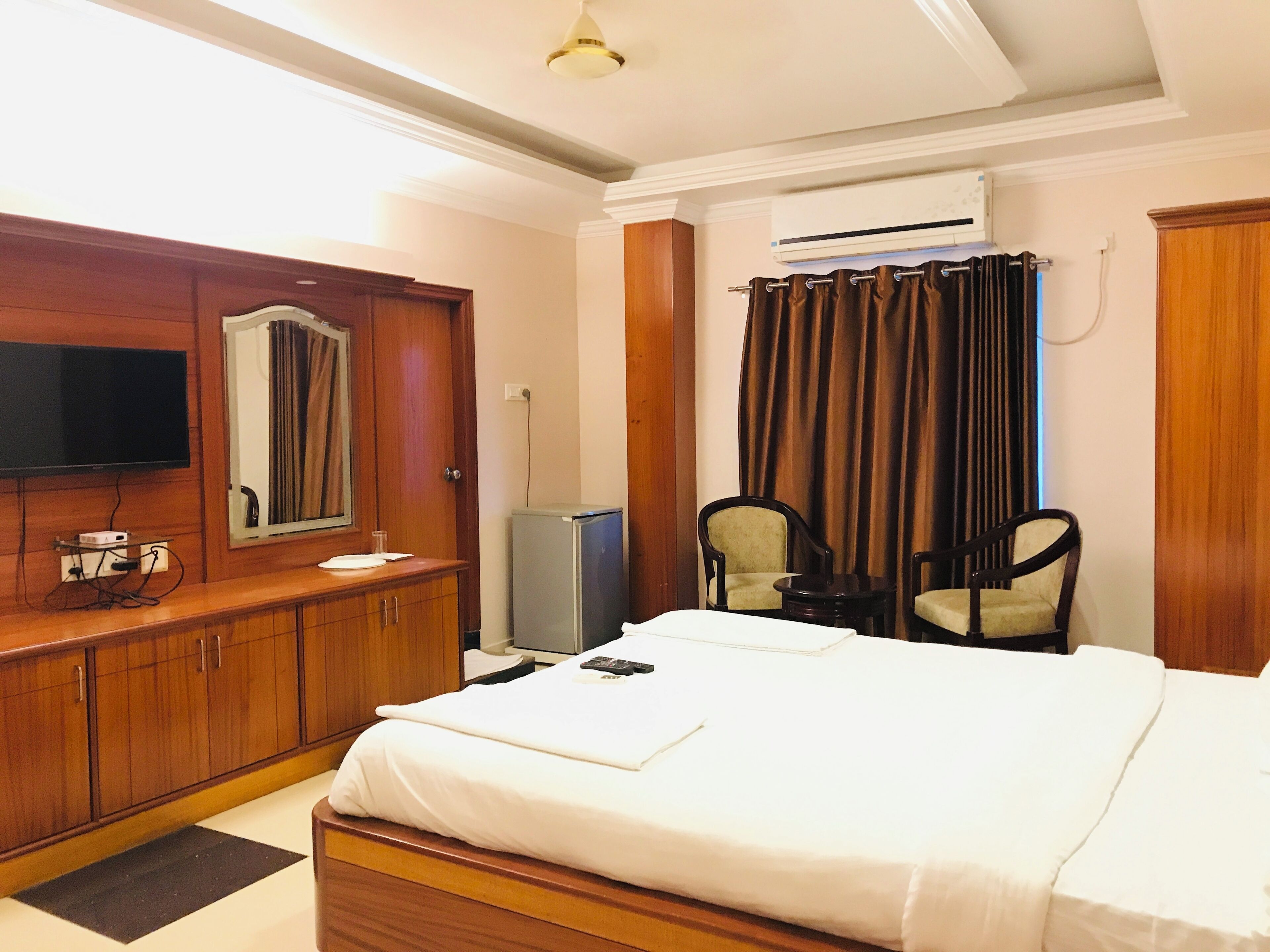 A hotel room with a bed, a TV, a wardrobe, a desk with a chair, and an air conditioning unit.