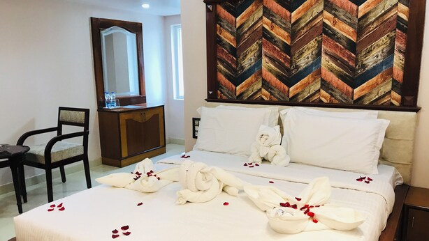 A hotel room with a bed, a wooden headboard, a mirror, a desk, and a chair. - NAVEED RESIDENCY (Anantapur)