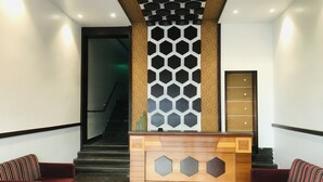A reception area with a wooden reception desk, two red sofas, a staircase, and a wall with a geometric pattern. - NAVEED RESIDENCY (Anantapur)