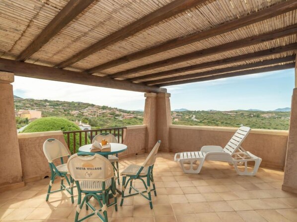 Un espacio de estar al aire libre cubierto con una mesa, sillas y un banco, con vistas a un paisaje montañoso.