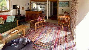 Una sala de estar acogedora con techo de madera, un sofá verde, una silla de madera, un tapete colorido y un sillón de peluche.