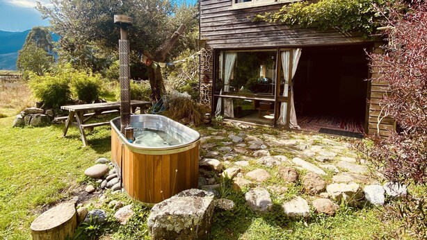 Una casa de madera rústica con jacuzzi, un sendero de piedra y vistas al paisaje.