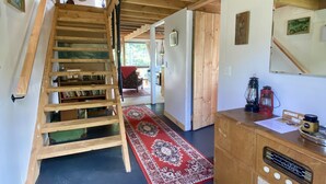 Una escalera de madera que conduce a una habitación con un tapete rojo estampado, una radio antigua y un armario de madera.
