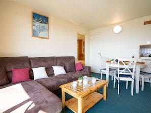 Ein gemütliches Wohnzimmer mit einer braunen Couch, einem Holztisch und einem Essbereich mit einem weißen Tisch und Stühlen.