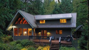 Une cabane à deux étages, dotée d’un toit en métal, de grandes fenêtres et d’une terrasse.