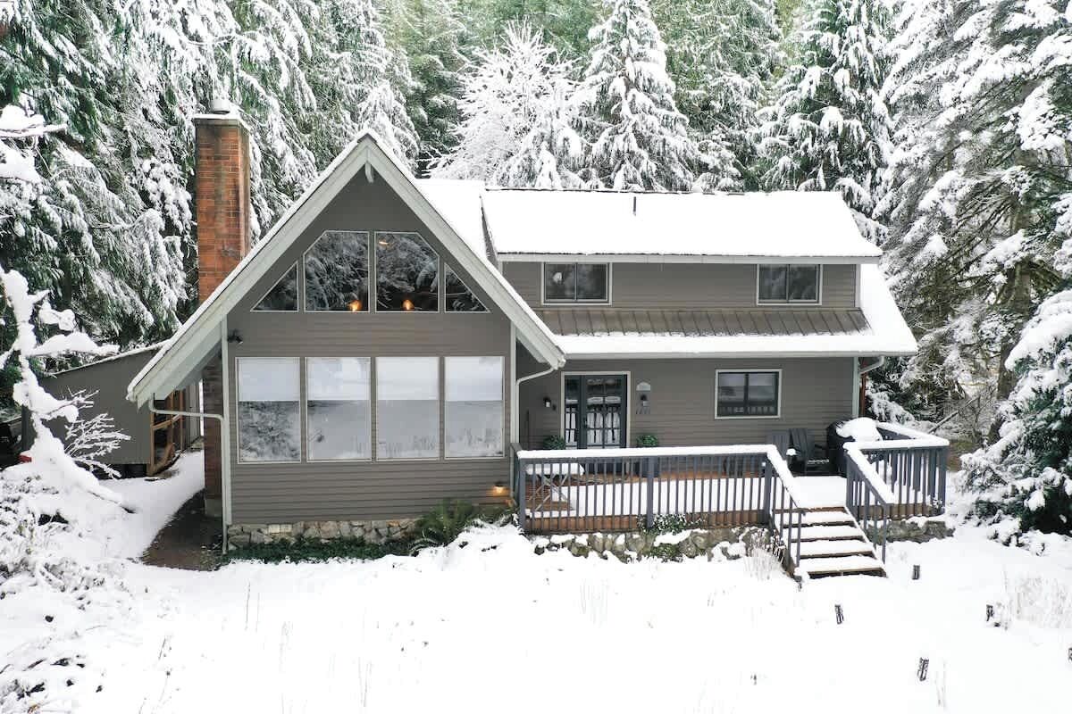 A two-story house with a front porch, surrounded by snow-covered trees.