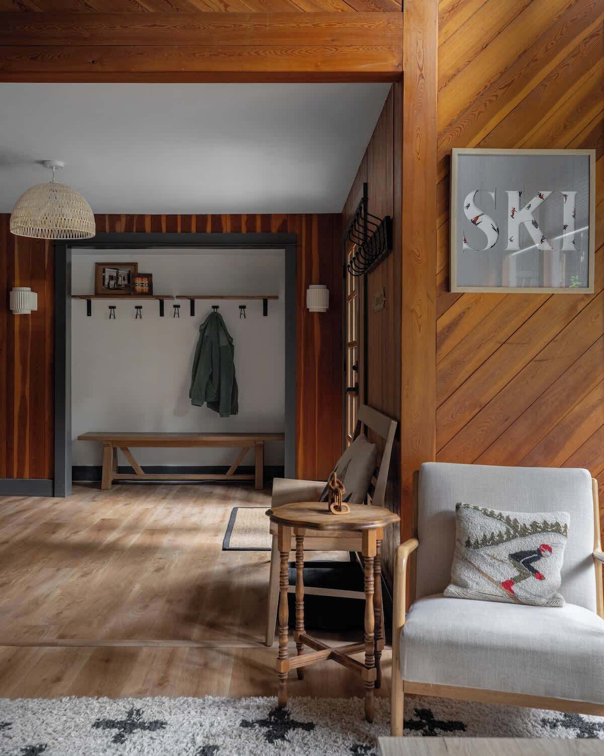 A wooden interior with a bench, a chair, a table, and a coat rack.