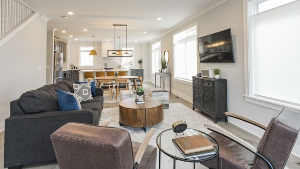 A spacious living room with a dark grey sofa, a round coffee table, and a television mounted on the wall. - Walk to Hip Bars* Photo wall* porch swings * designer home*  (B) (Nashville)