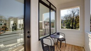 A balcony with two chairs and a table, large windows, and a view of trees and houses. - Walk to Hip Bars* Photo wall* porch swings * designer home*  (B) (Nashville)