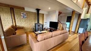 Amplia sala de estar con pared de piedra, un sofá, un televisor y una mesa de comedor de madera.
