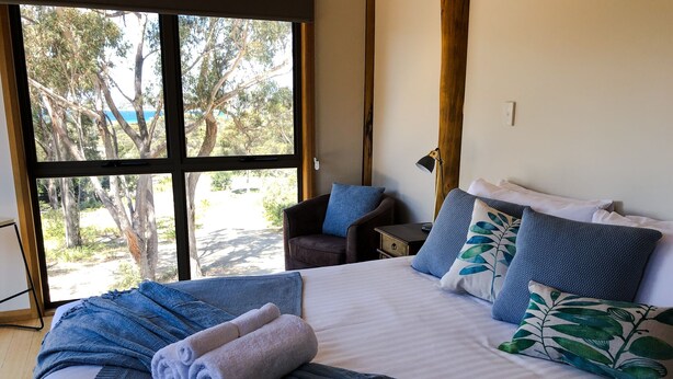 Un dormitorio con una cama grande, vistas a árboles a través de una ventana y una silla con un cojín.
