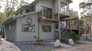 Una casa de dos pisos con balcón, una escalera y un pequeño jardín con rocas y plantas.
