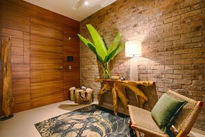 A room with a wooden wardrobe, a plant on a wooden stand, a woven chair, and a patterned rug.