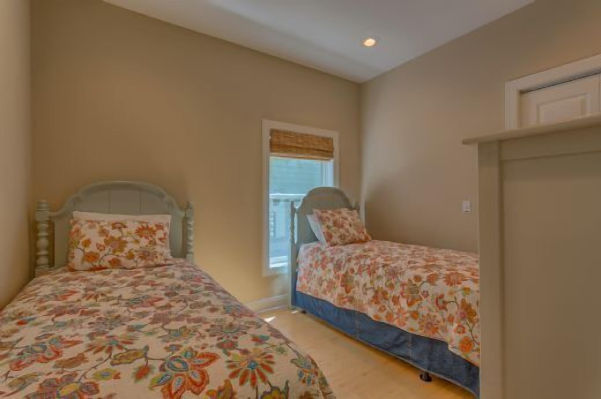 A bedroom with two single beds, a window with a blind, and a door.