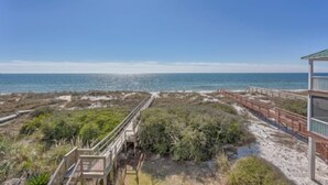 Une plage avec une vue sur une promenade en bois menant à un bâtiment doté d’un balcon donnant sur l’océan.