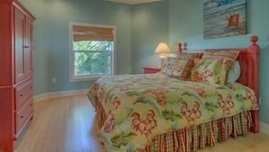 Une chambre à coucher avec un lit, une fenêtre avec des stores, un ventilateur de plafond et un tableau au mur.