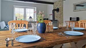 A dining area with a wooden table set for four, a blue vase with flowers, and a stone wall in the background.