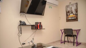 A hotel room with a desk, a chair, a mounted TV, a phone, and a poster on the wall. - King One bedroom AC HOT TUB ELEVATOR 2 Flat screens (Medellin)