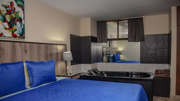 A hotel room with a bed, a nightstand, a lamp, a sink, and a mirror. - King One bedroom AC HOT TUB ELEVATOR 2 Flat screens (Medellin)