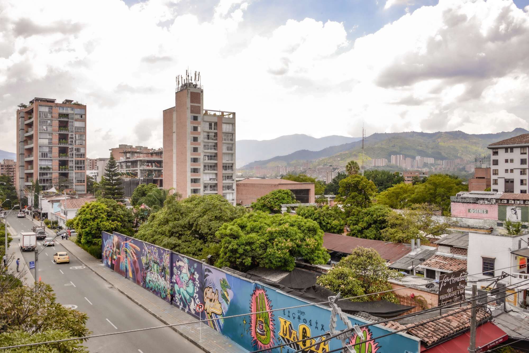 Une vue urbaine avec de hauts immeubles, une route où circulent des véhicules et une fresque colorée sur un mur.
