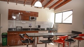A modern kitchen with wooden cabinets, a stainless steel countertop, a microwave, a gas stove, and a bar area with red and black bar stools. - 5 Bed PH ENTIRE ROOF HOT TUB ELEVATOR Private roof Guests with Photo ID (Medellin)