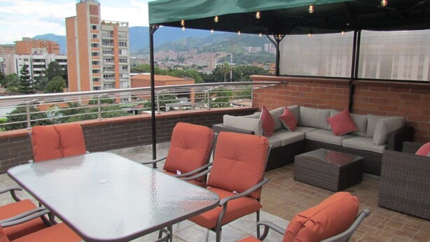 An outdoor patio with a glass table and orange chairs, a gray sofa with red cushions, and a brick wall. - 5 Bed PH ENTIRE ROOF HOT TUB ELEVATOR Private roof Guests with Photo ID (Medellin)