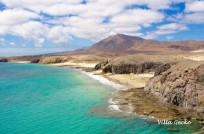 A coastal landscape with a beach, clear turquoise waters, and rocky cliffs.