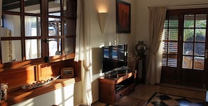 A living room with a television, wooden furniture, a window with curtains, and a tiled floor.