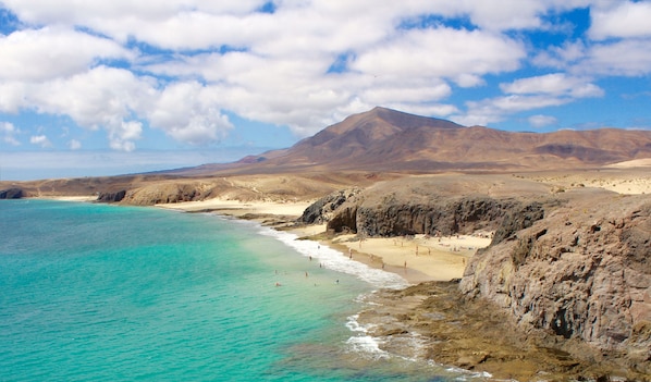 A coastal landscape with a beach, clear turquoise waters, and rocky cliffs.