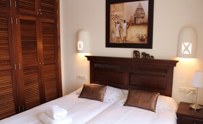 A neatly made bed with two pillows, a wooden headboard, and a framed painting above it.