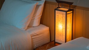 Cama bem arrumada com lençóis brancos e uma luminária de parede estilo lanterna.