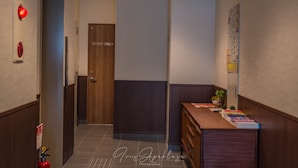 Um corredor com uma porta de madeira identificada com a inscrição “STAFF ONLY”, um alarme de incêndio e uma mesa de madeira com livros e uma pequena planta.