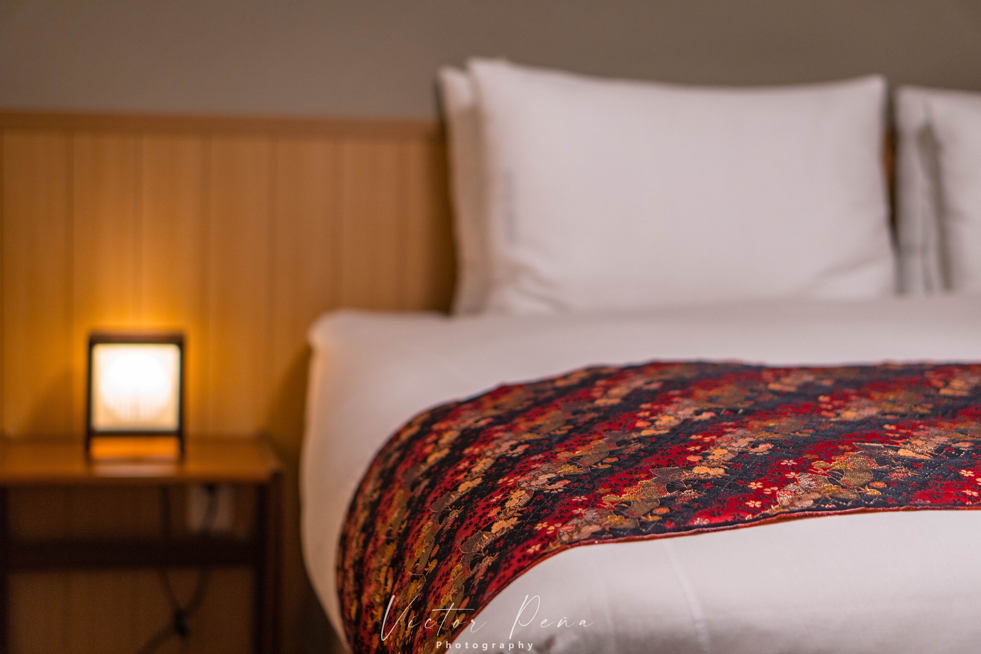 A hotel room with a bed, a nightstand, and a lamp.