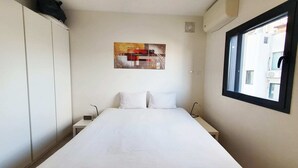 Een hotelkamer met een bed, nachtkastje, kledingkast en een raam met uitzicht op gebouwen.