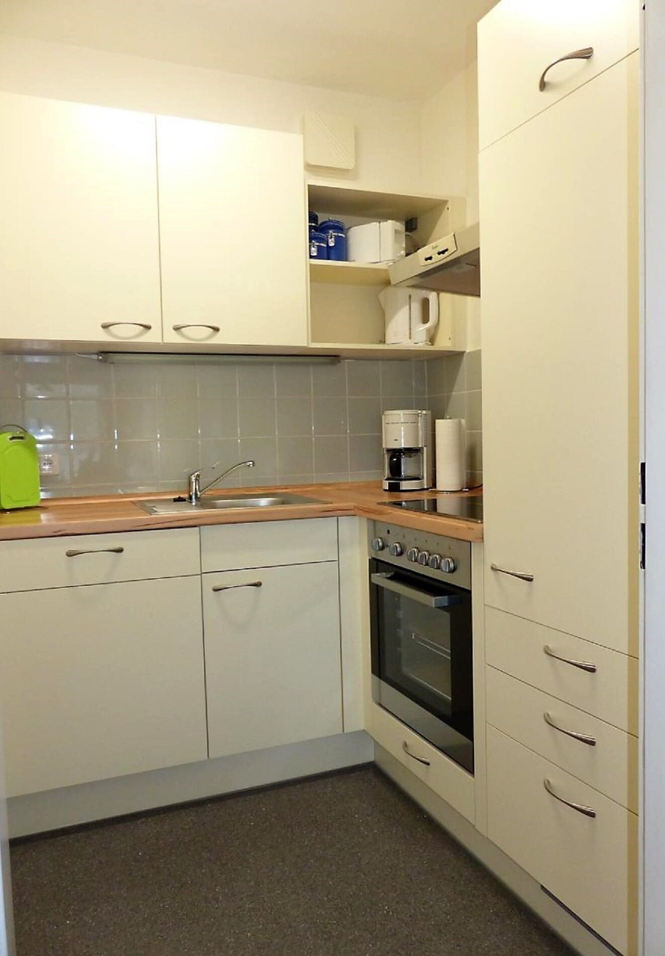 A compact kitchen with white cabinets, a stainless steel sink, a built-in oven, and a coffee maker on the countertop.
