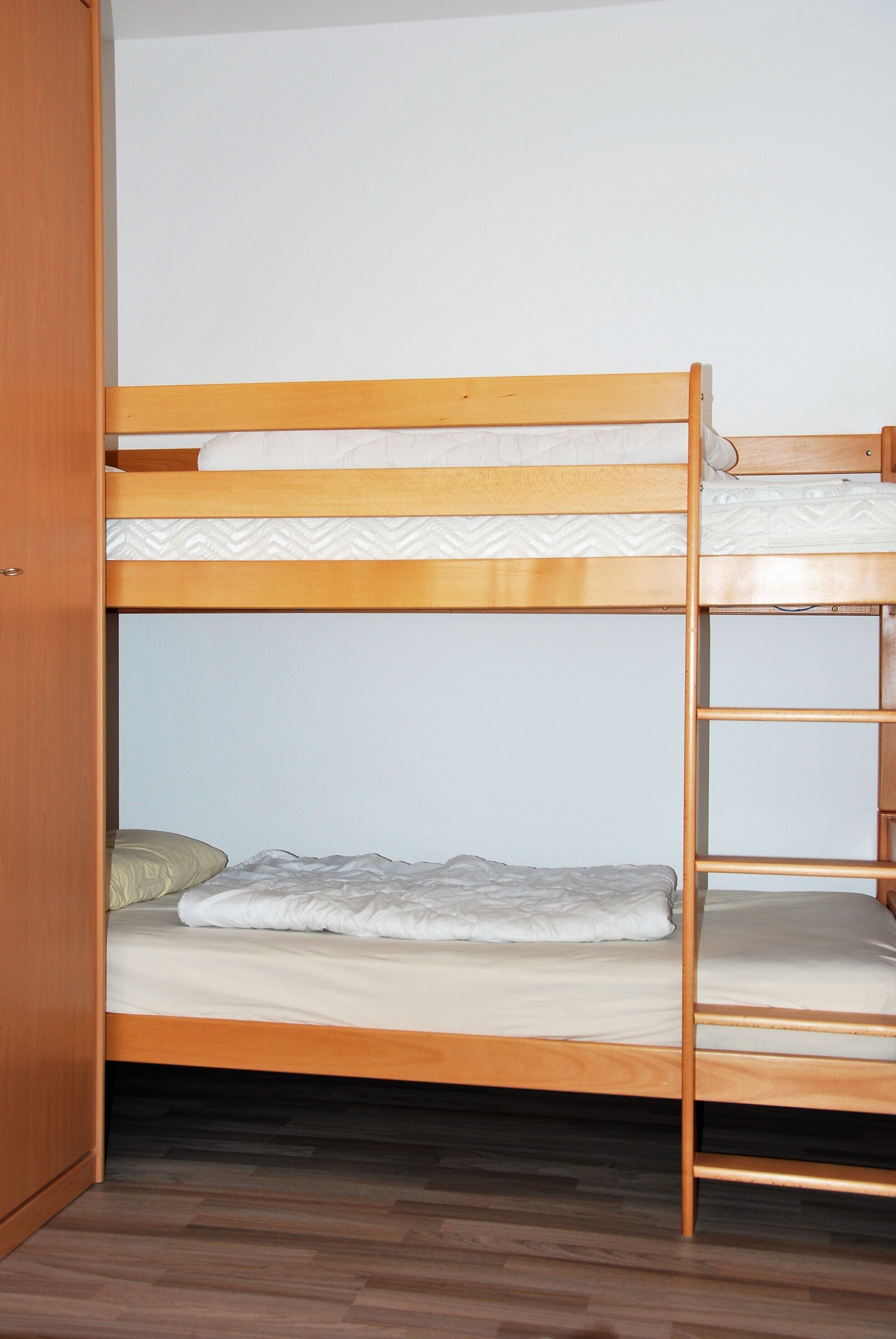 Una cama de solapada con escalera de madera, un armario y suelo de madera.