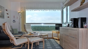 A modern living room with a sofa, two chairs, a small table, and a kitchen area with a coffee machine. - Frische Brise (Cuxhaven)