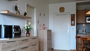 A modern kitchen with a microwave, toaster, and coffee maker. There is a wooden cabinet with drawers and a vase with flowers on the counter. - Frische Brise (Cuxhaven)