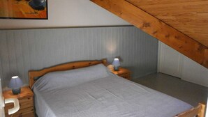 A bedroom with a sloped ceiling, a bed with a grey mattress, wooden headboard, two bedside tables with lamps, and a painting on the wall.