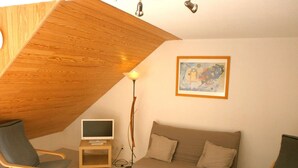A cozy living room with a slanted ceiling, a flat-screen TV, a sofa, two armchairs, and a coffee table.
