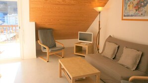 Ein gemütliches Wohnzimmer mit Holzboden, einem grauen Sessel, einem beigen Sofa, einem kleinen Holztisch und einer Stehlampe.
