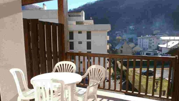 A balcony with white plastic chairs and a table, overlooking a residential area with houses and a mountain in the background.